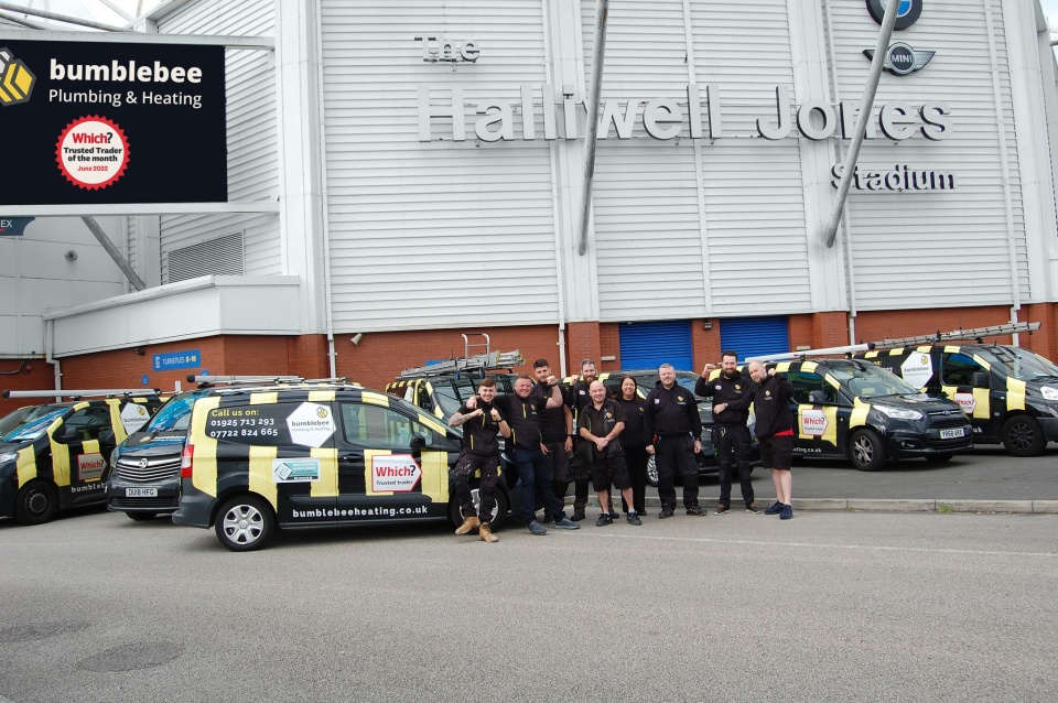 A group of people stood outside a stadium, in front of lots of vans with the Bumblebee Heating logo and colourings on.