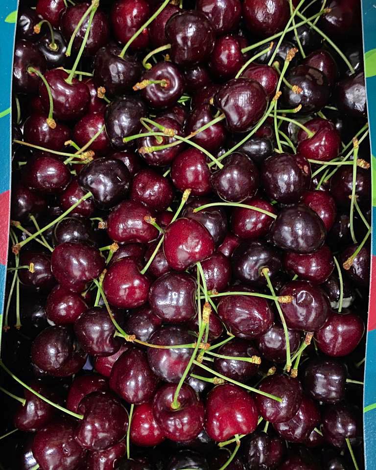 A box of ripe, dark-red cherries, with reflections on from the light.
