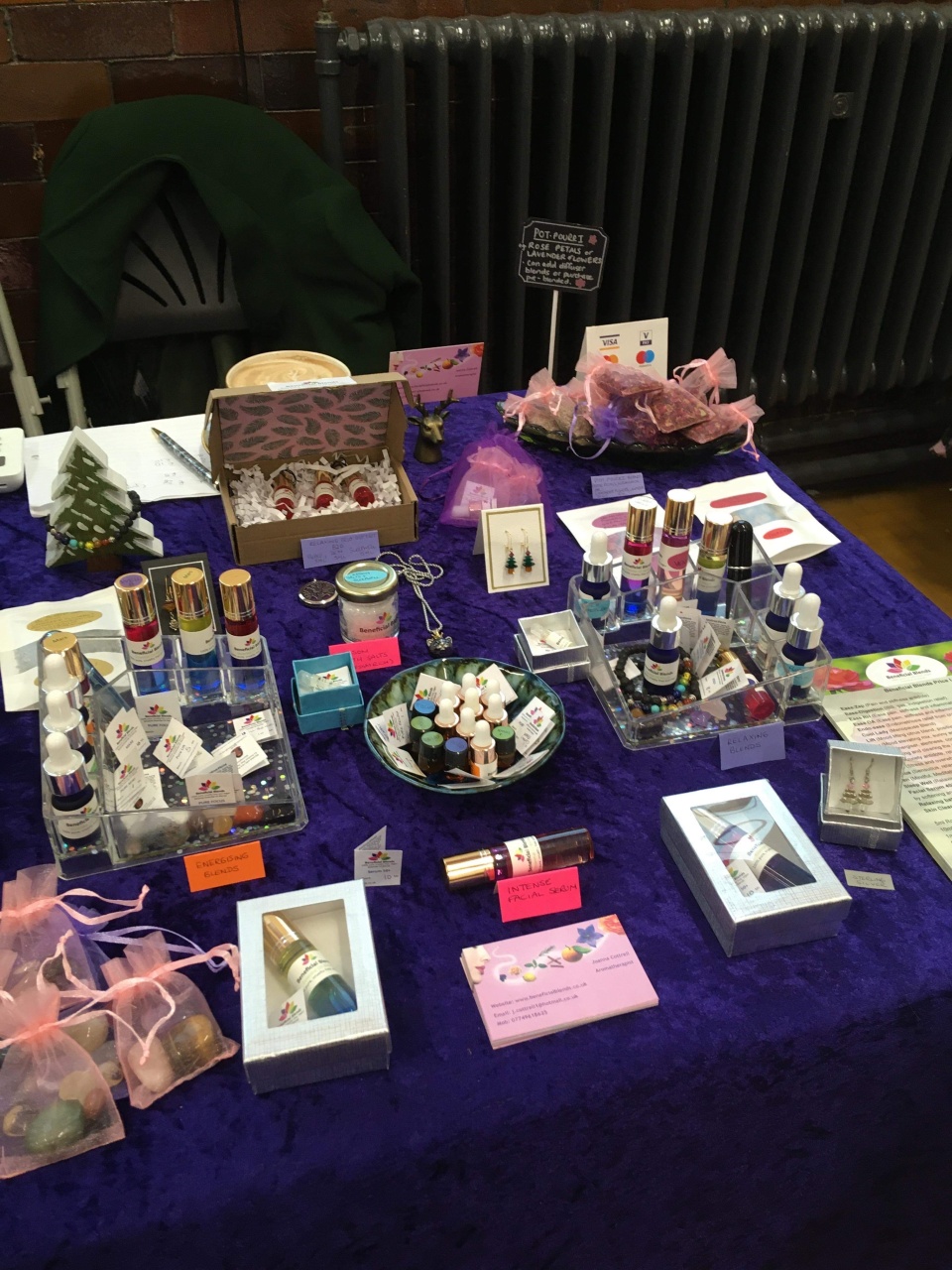 essential oils photographed being sold at a wellbeing fair, the stall has a purple clothed table, lots of different blends and also some jewellery