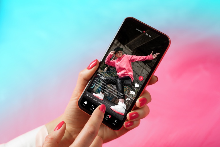 TikTok application shown on a phone screen (with a young person dancing to hip hop). Placed on a blue to pink gradient background.